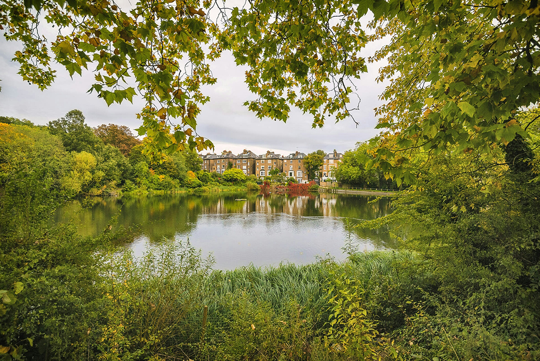 Plano general de un lago y unas casas de estilo inglés al fondo