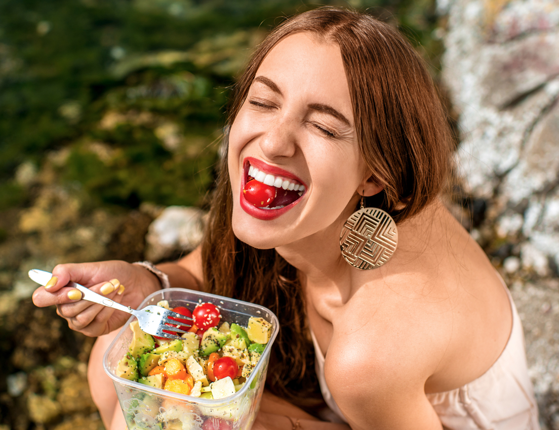 Plano picado de una mujer joven comiendo una ensalada con tomatitos cherry al aire libre