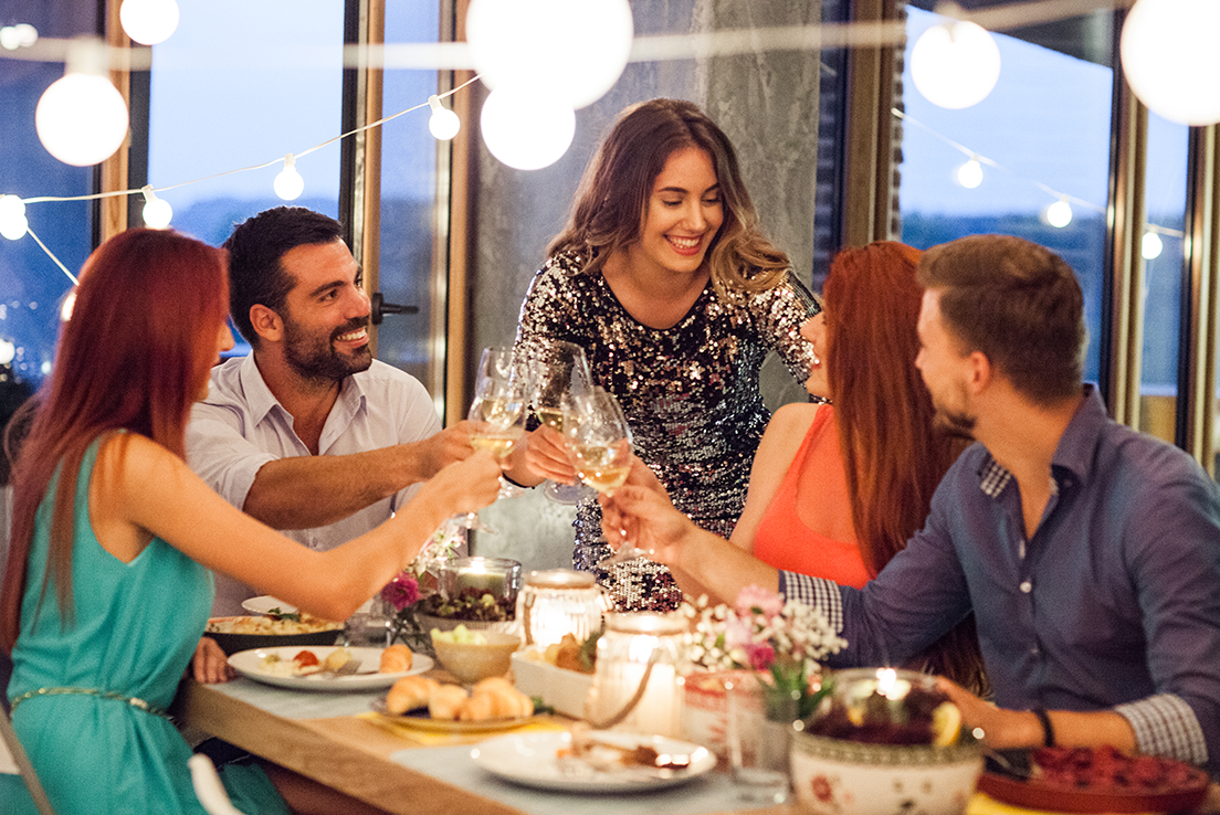 Grupo de hombres y mujeres brindando en una mesa con copas de vino blanco