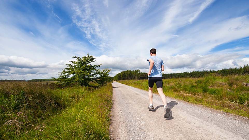 imagen de un chico haciendo running en campo con cielo azul con nubes