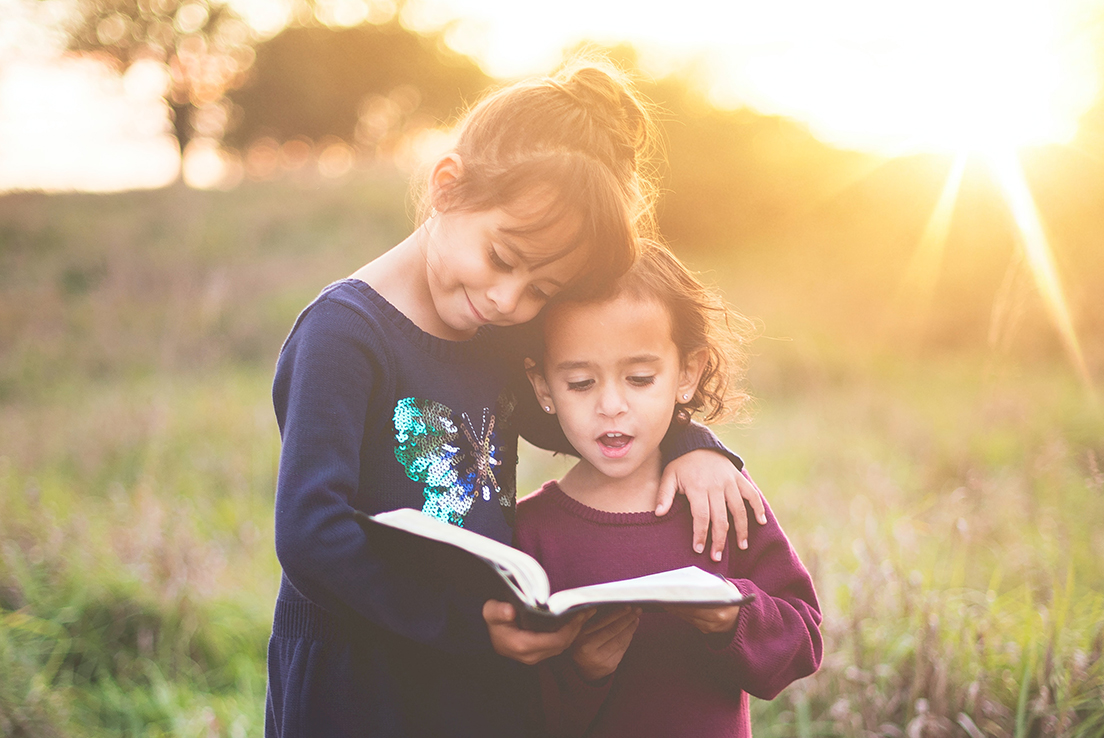 imagen de dos niñas leyendo un libro juntas en el campo